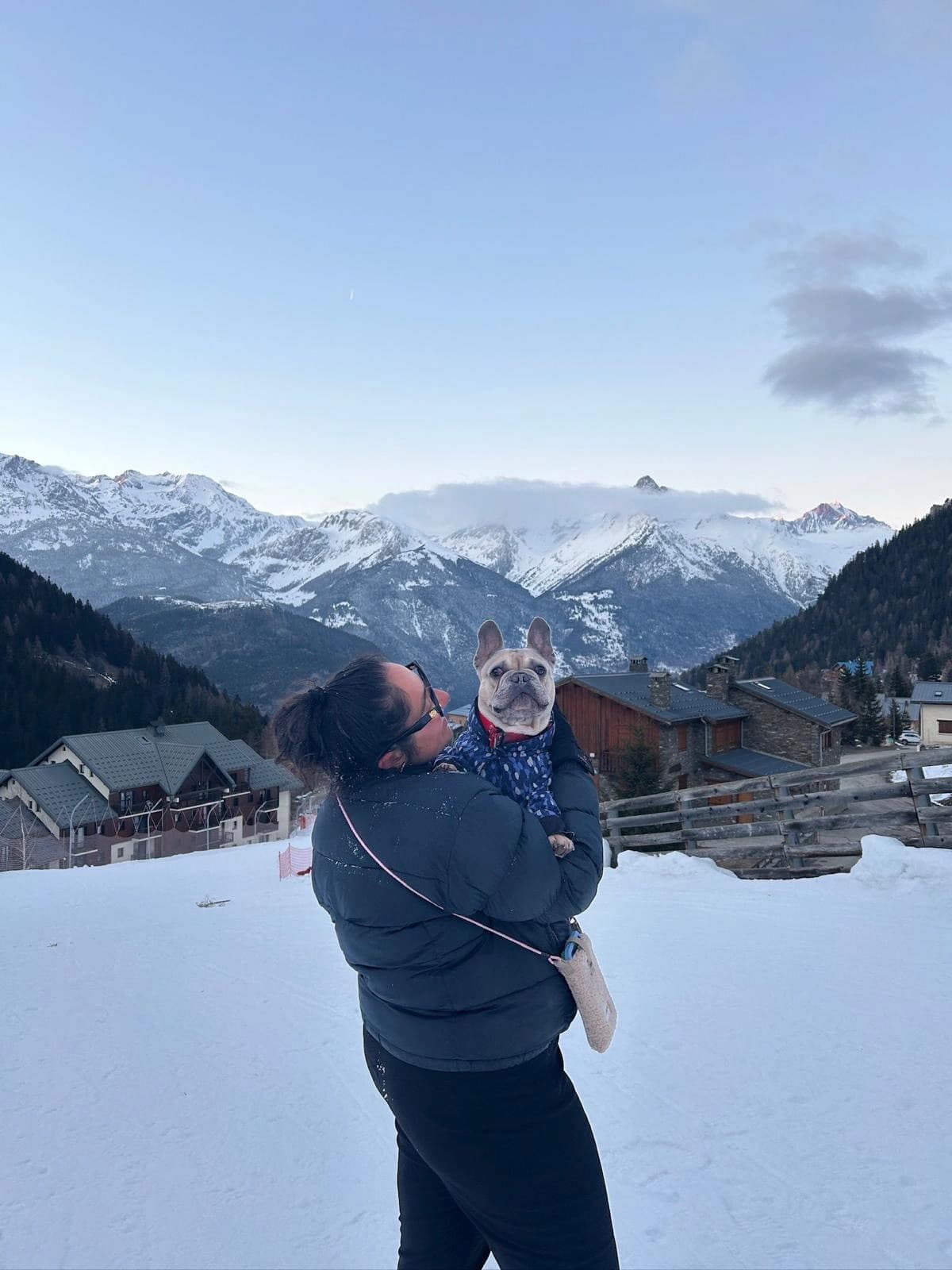 Une accompagnatrice serre un bouledogue en manteau, face aux montagnes