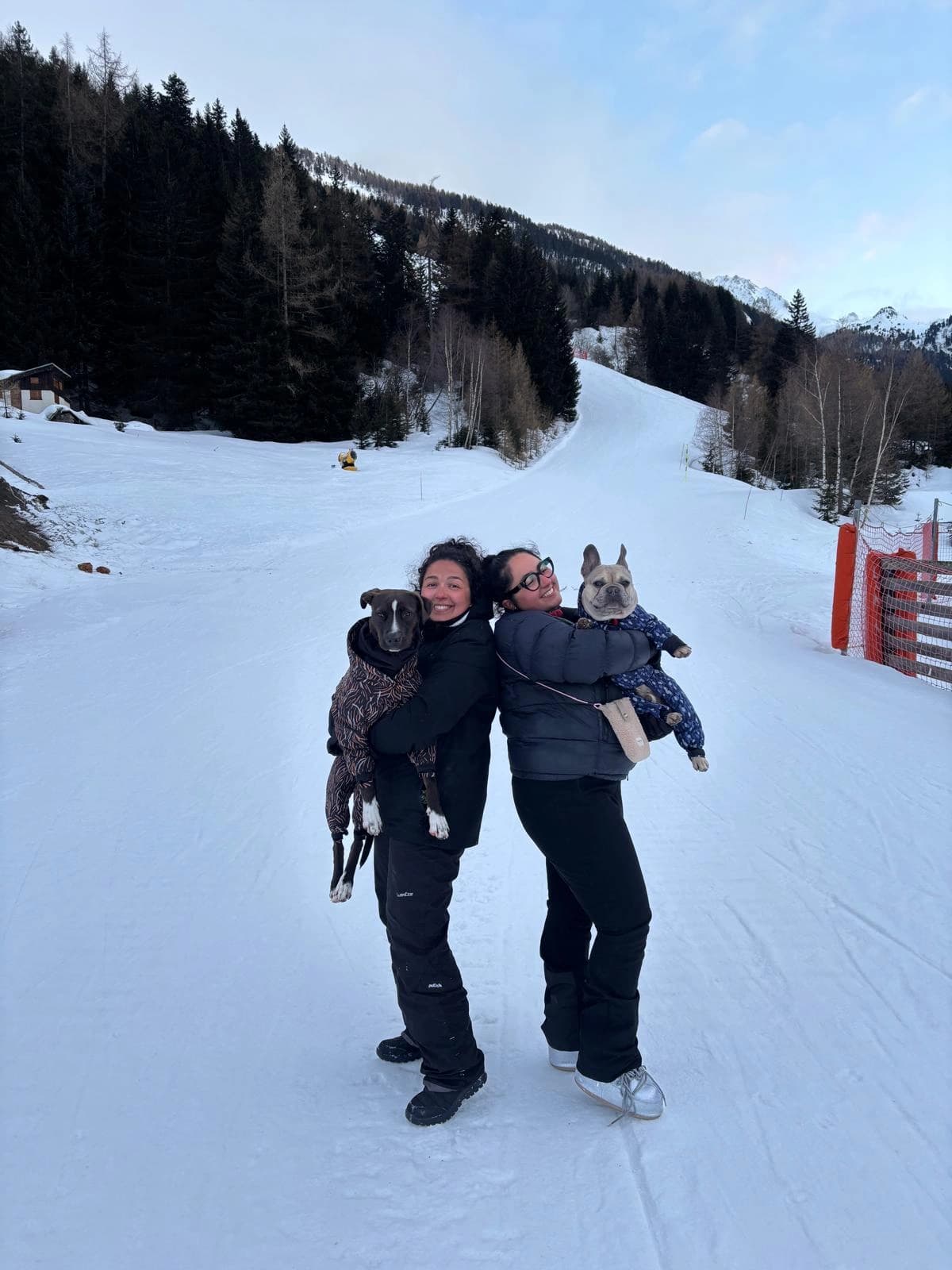 Deux accompagnatrices portent chacune un chien sur une piste enneigée