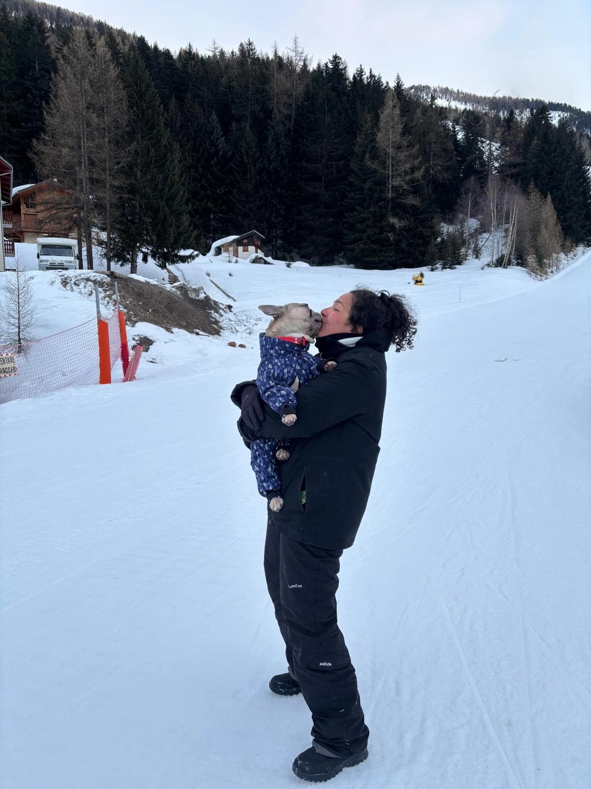 Une accompagnatrice fait un bisou à un chien en manteau sur le chemin enneigé