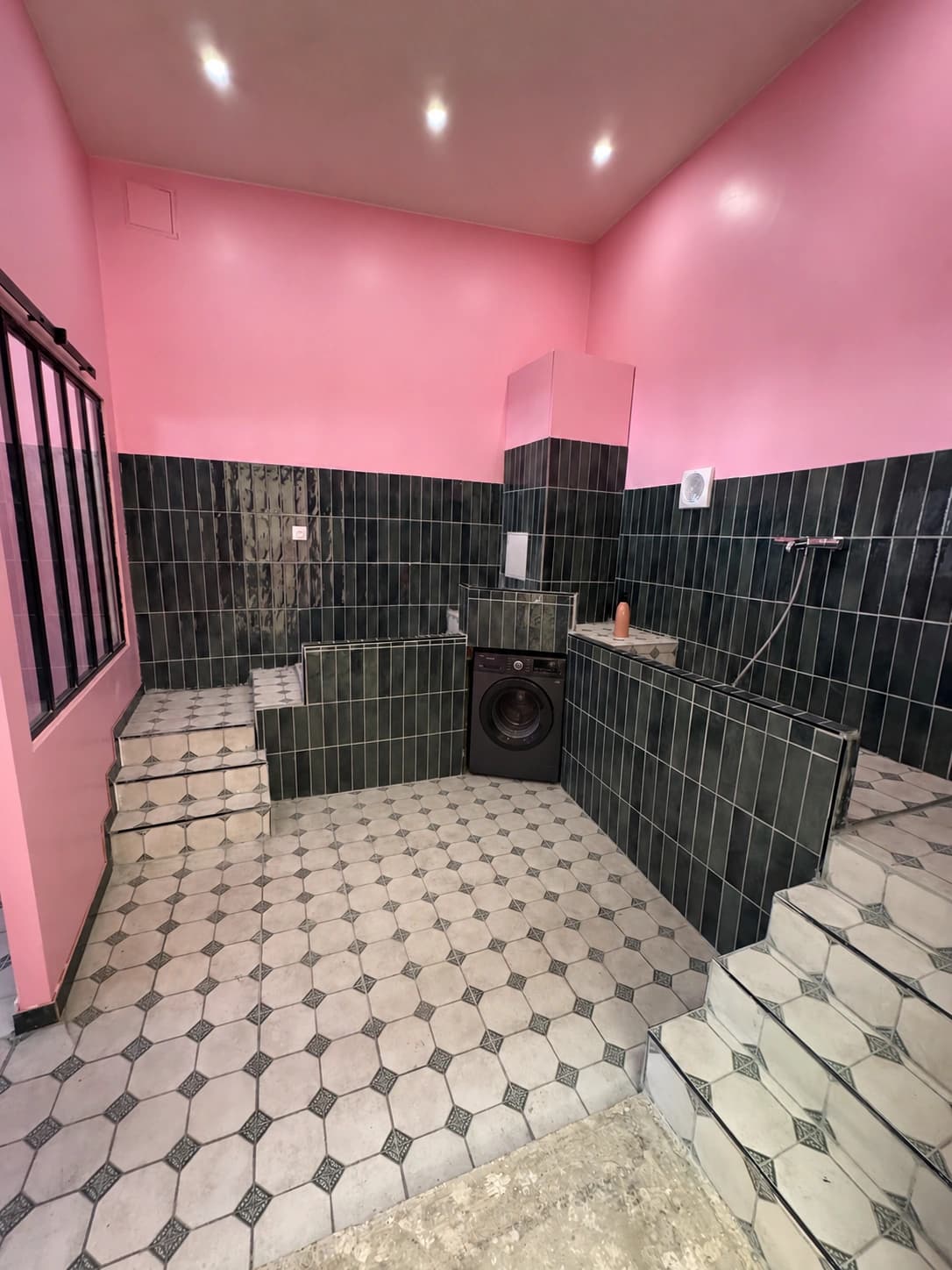 La salle de lavage du Dog Wash : murs roses, carrelage sombre et douche